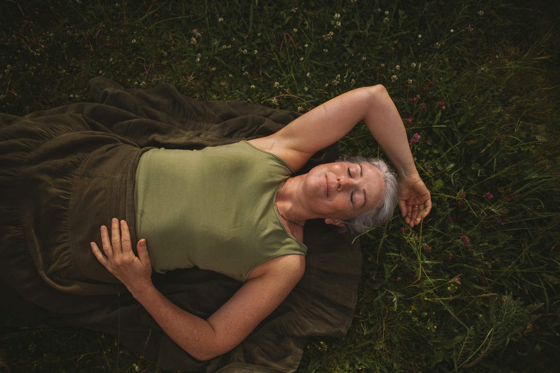 Ruth lying back in long grass with wildflowers, one arm resting behind her head, at rest