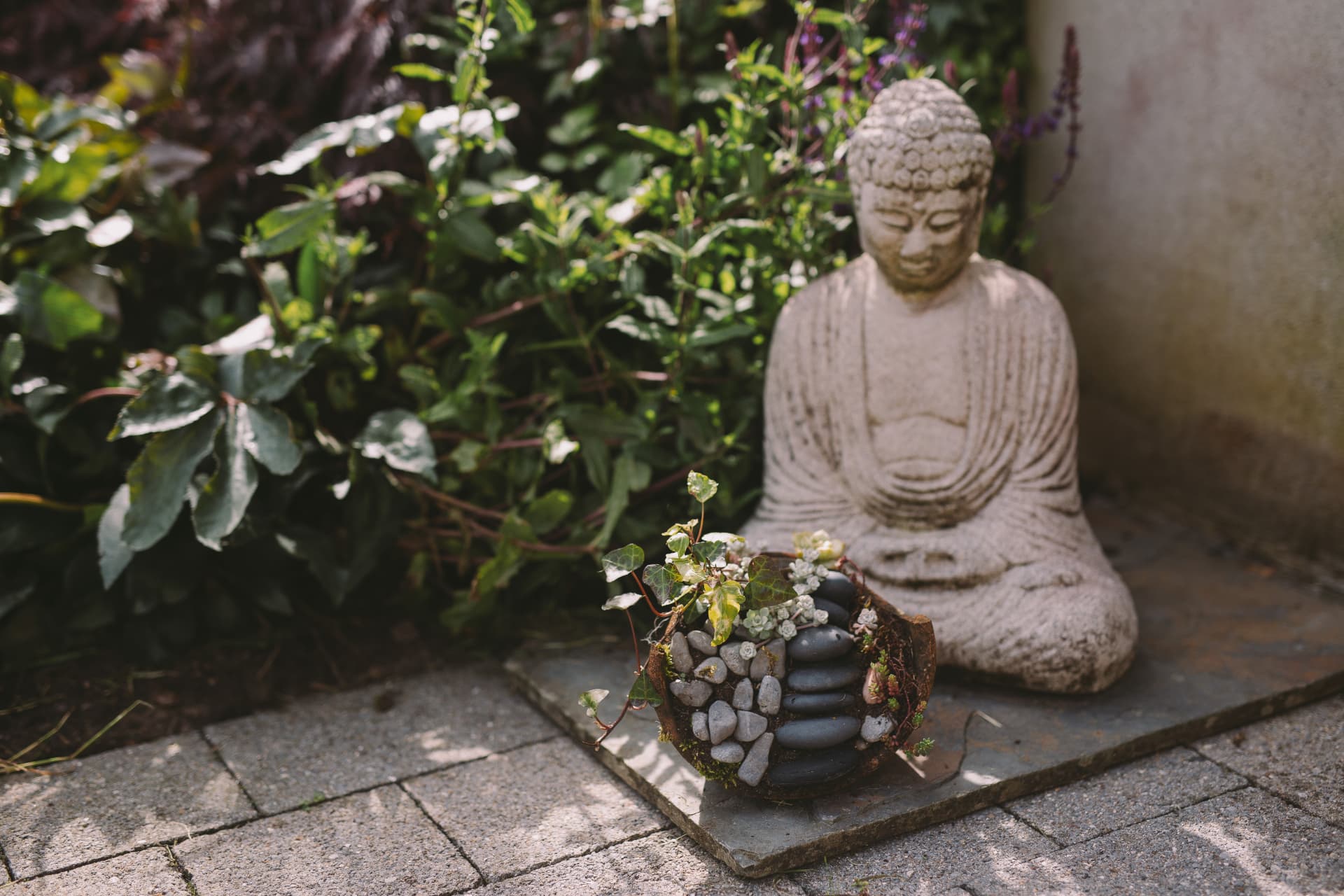 Stone Buddha in the garden beside a bowl of pebbles and ivy