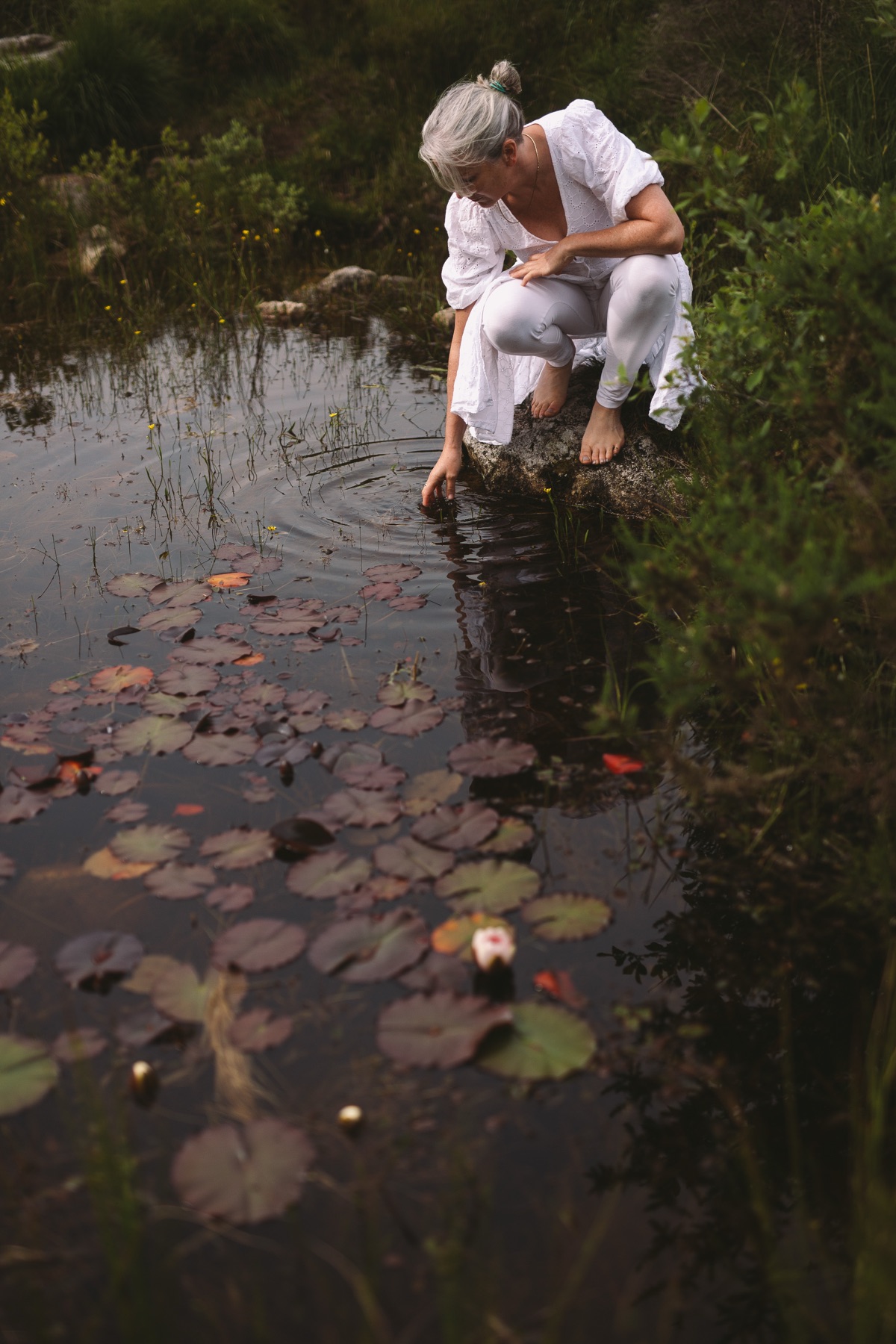 Ruth crouching at the edge of a still pond among lily pads