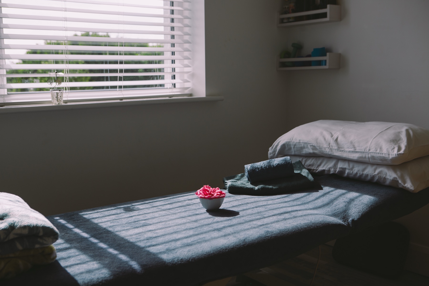 The treatment room in warm afternoon light, blanket and a bowl of pink flowers