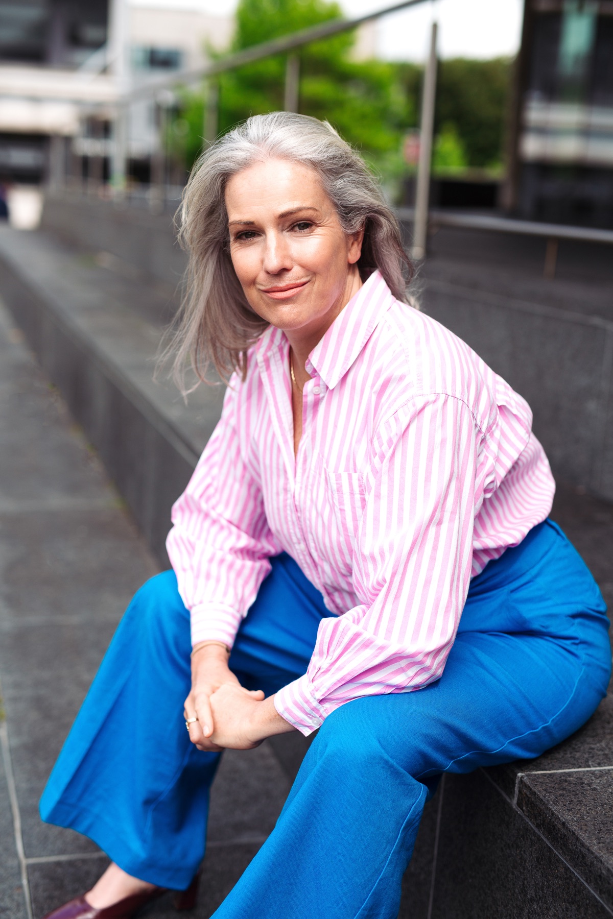 Ruth Molloy, seated portrait, pink striped shirt and blue trousers