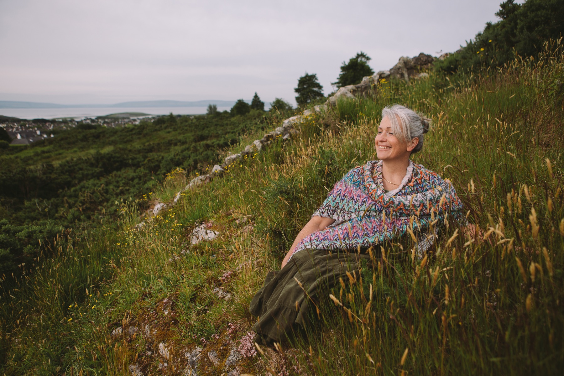 Ruth sitting in a hillside meadow above the coast, at golden hour